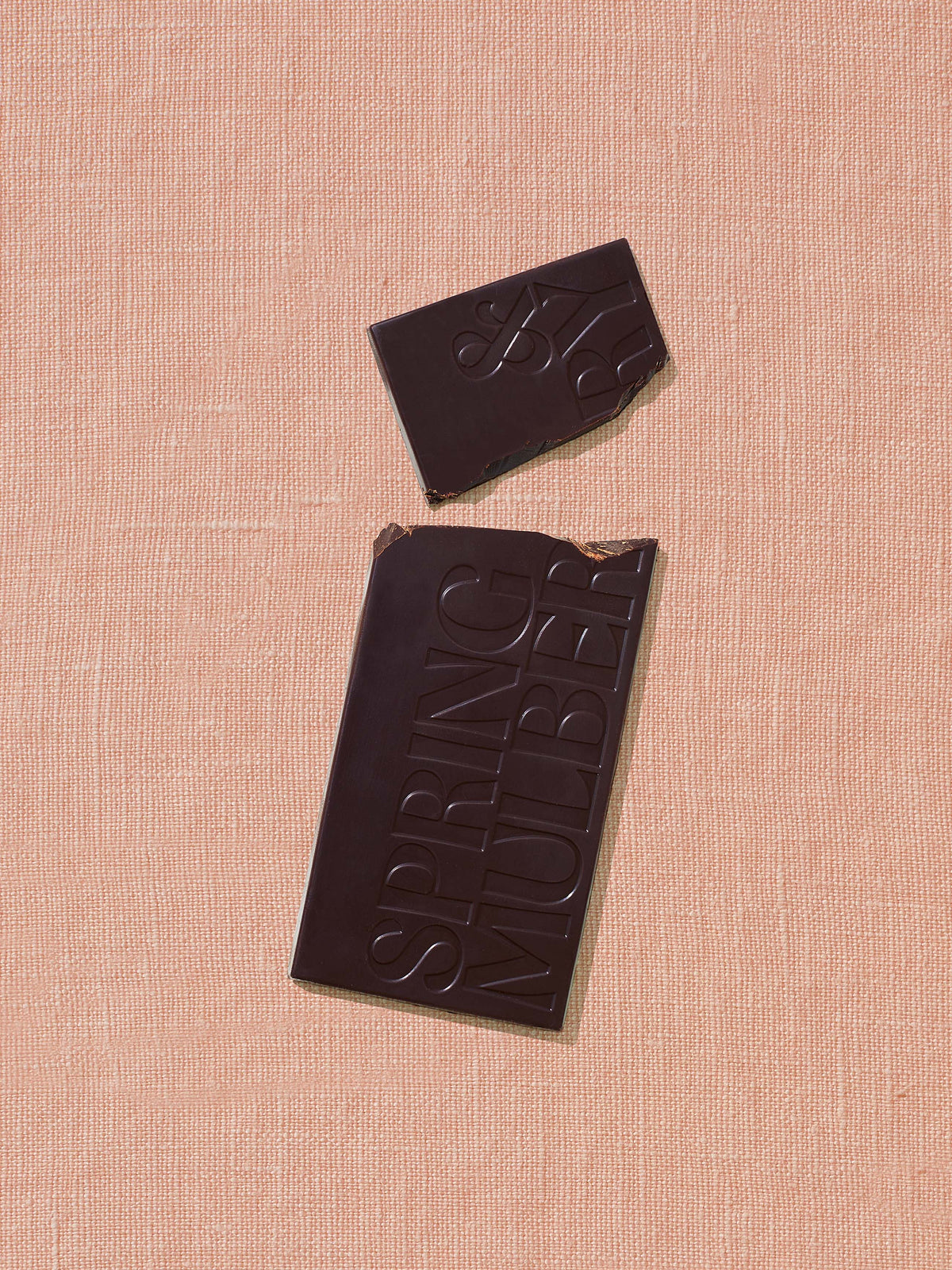 Dark chocolate bar with a piece missing on a pink textured background