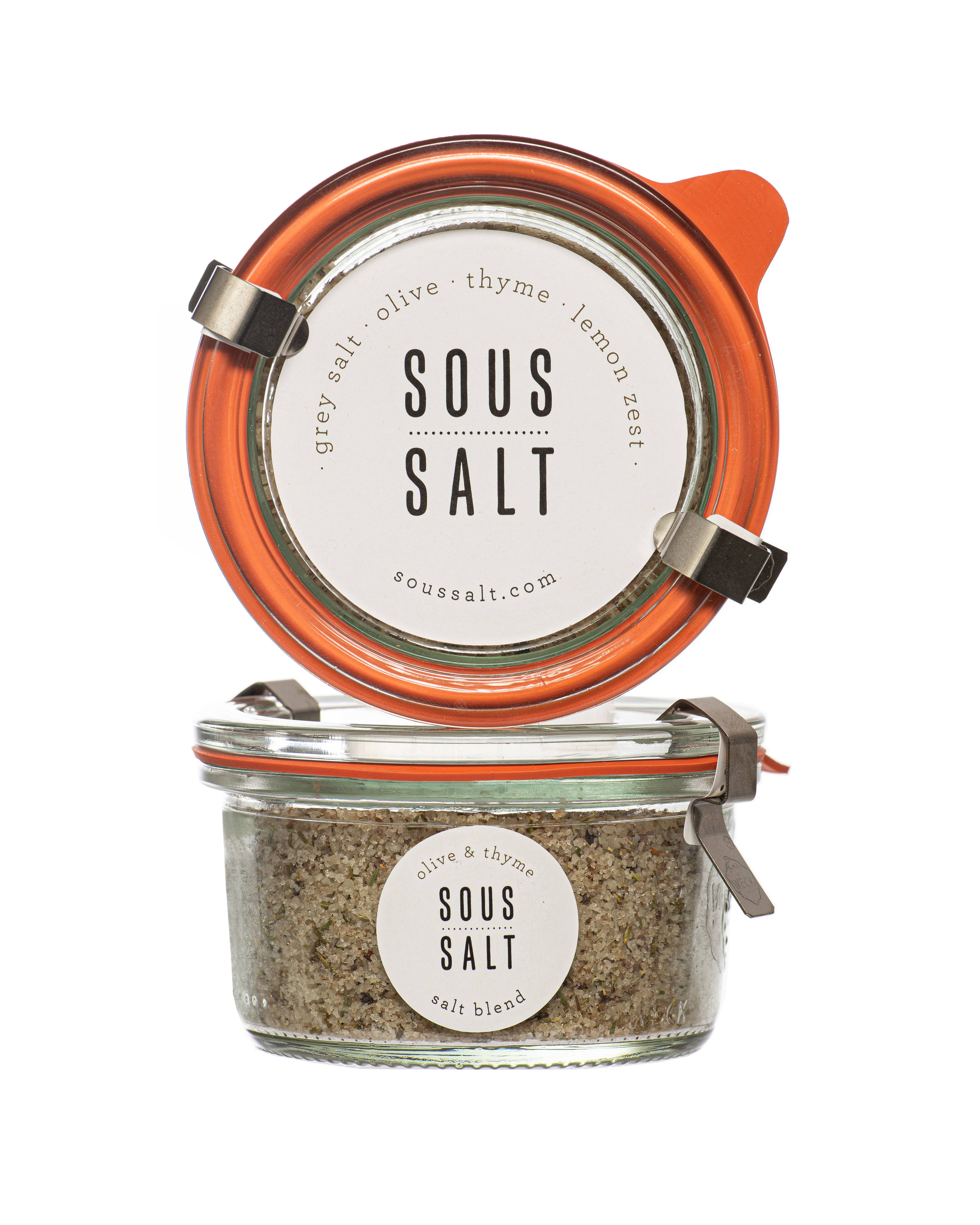 Glass jar of Grey Salt, Olive, and Thyme condiment by Sous Salt, featuring a clear jar with grey salt and herbs inside.