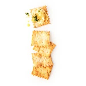 Rustic Bakery Olive Oil & Sel Gris Crackers on a wooden surface, showcasing their crispy texture and golden-brown appearance.