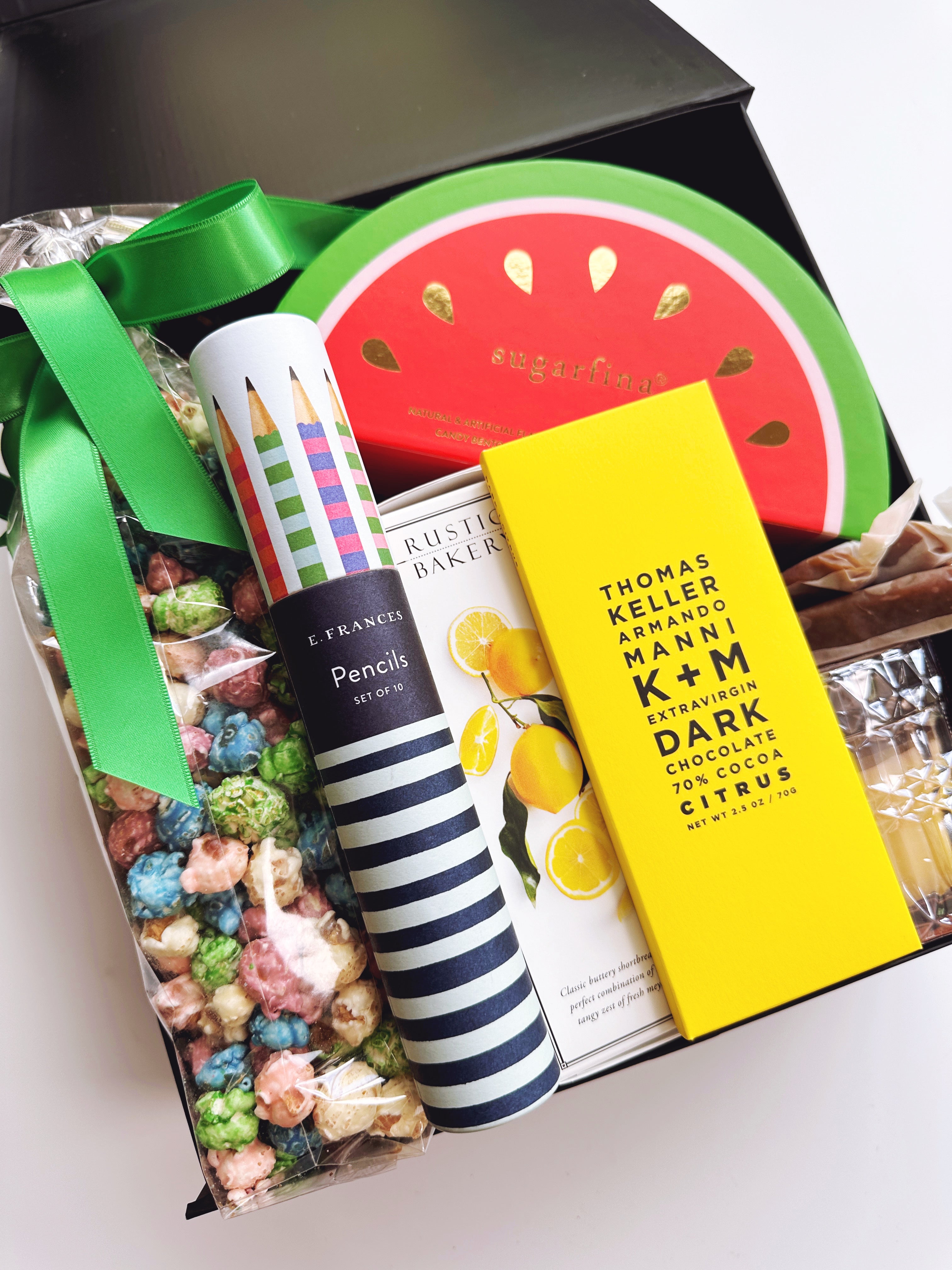 Gift box with colorful popcorn, striped pencils, and a chocolate bar.