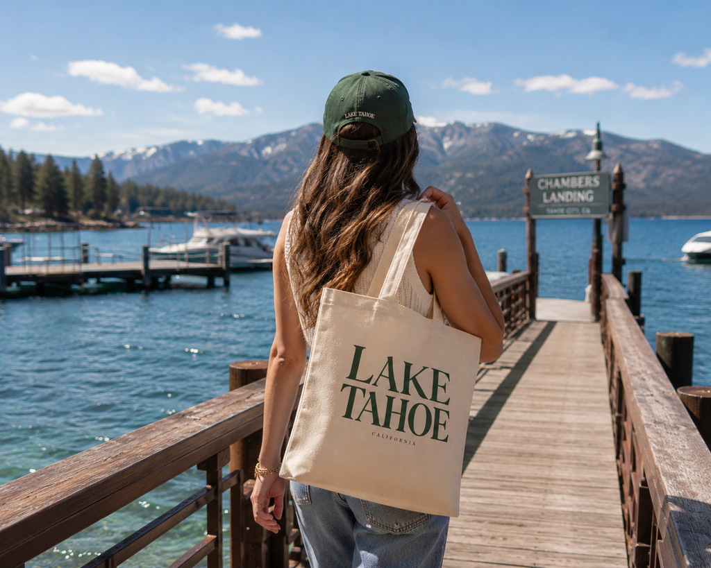 Person holding a 'Lake Tahoe' tote bag on a dock with a scenic background
