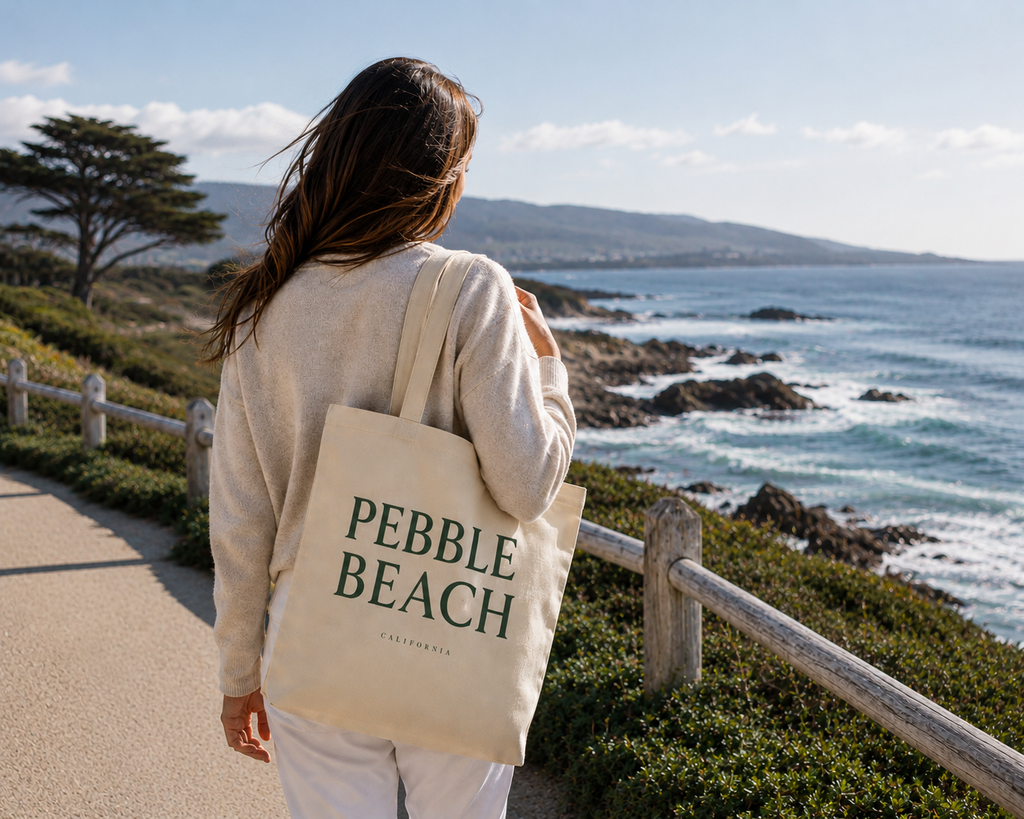 Person holding a 'Pebble Beach' tote bag walking along a coastal path.