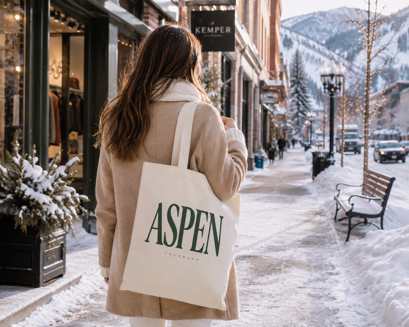 Person holding a tote bag with 'Aspen' on it, walking down a snowy street in a mountain town.