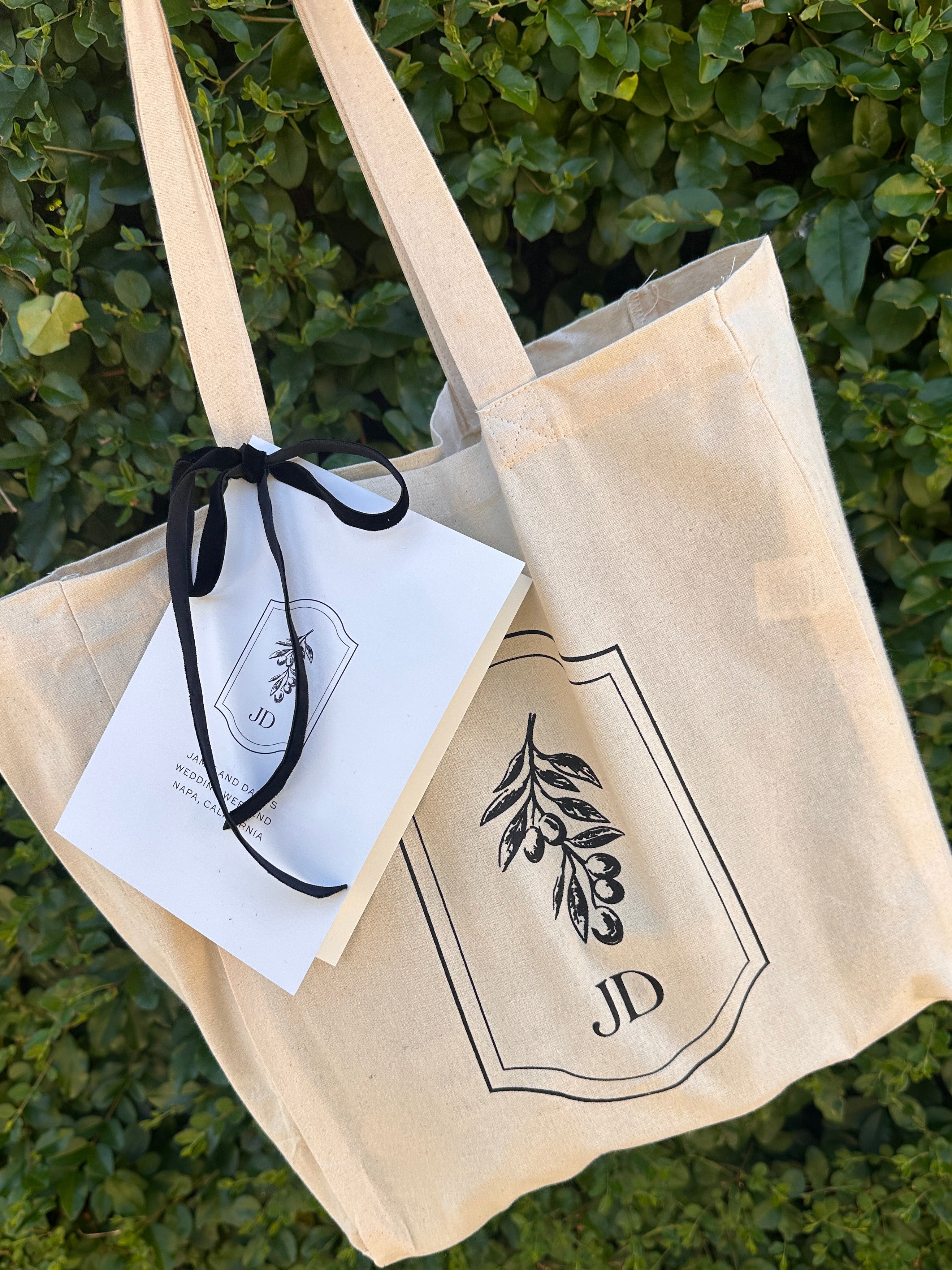Beige tote bag with black logo on a green leafy background