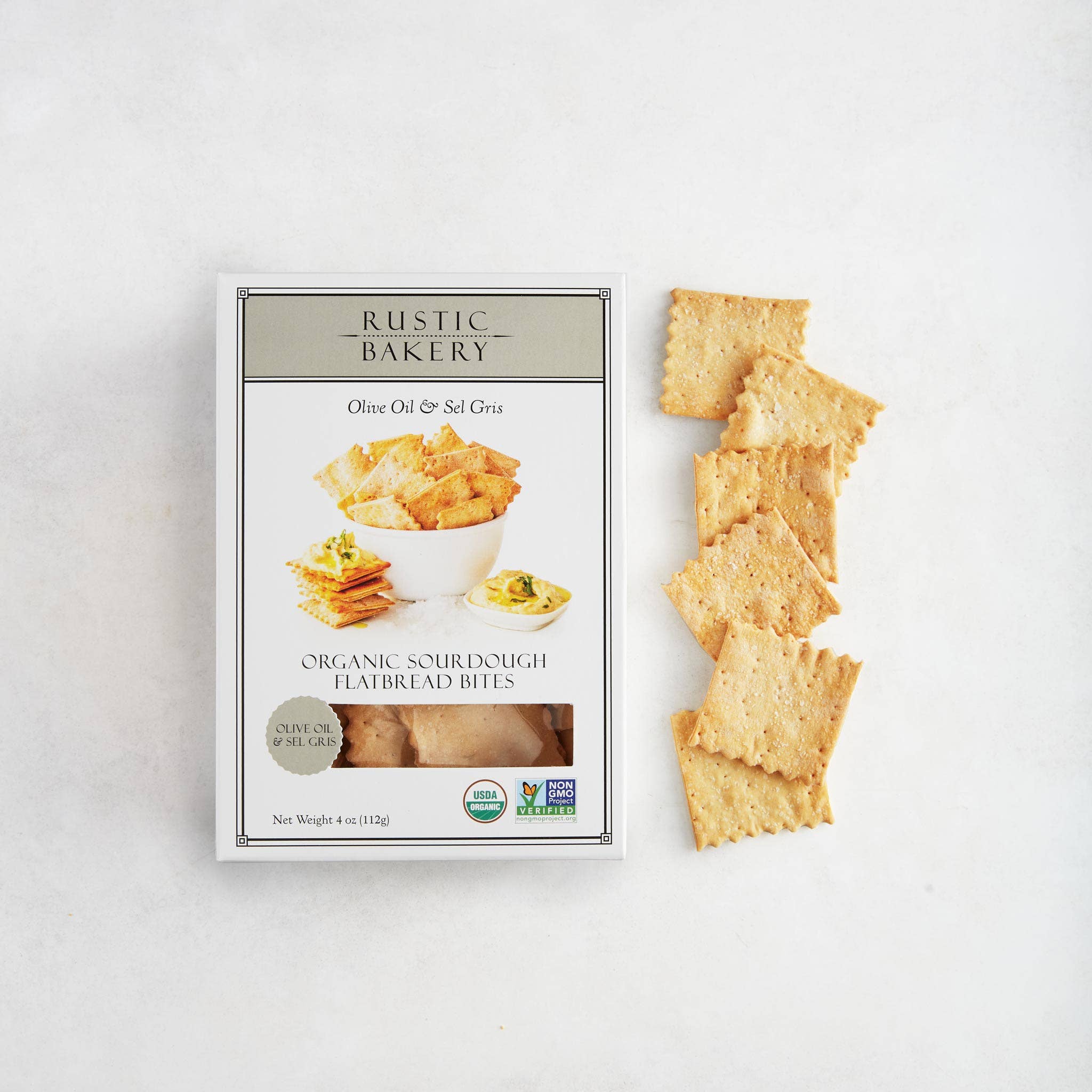 Rustic Bakery Olive Oil & Sel Gris Crackers in a bowl with some crackers stacked nearby on a rustic wooden surface.